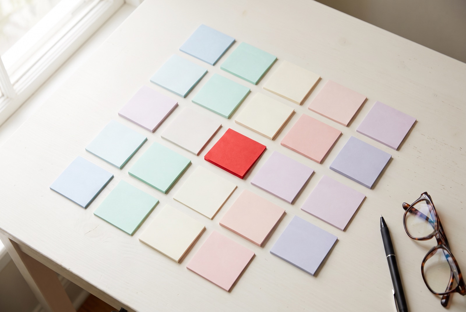 A grid of small blank sticky notes on a pale desk, one red note standing out
