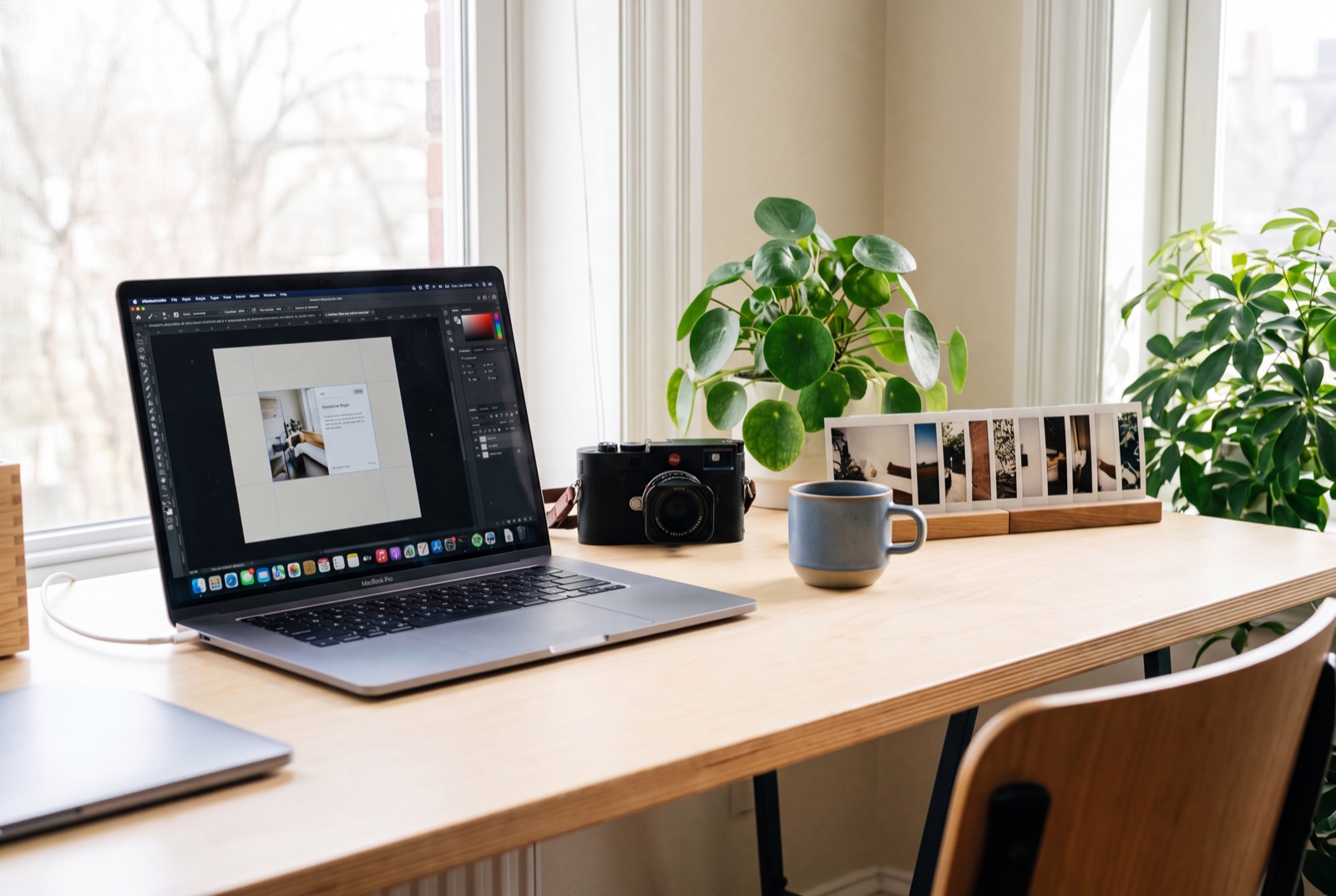 A tidy creative desk with a laptop, camera and a row of printed photos