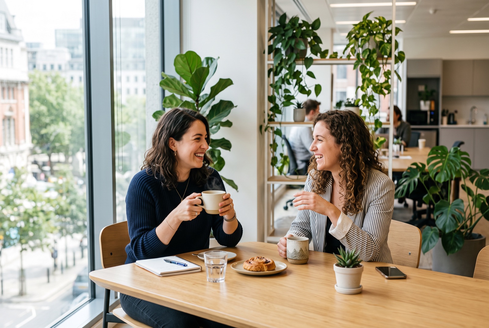 Two colleagues having a friendly conversation over coffee at a bright office table